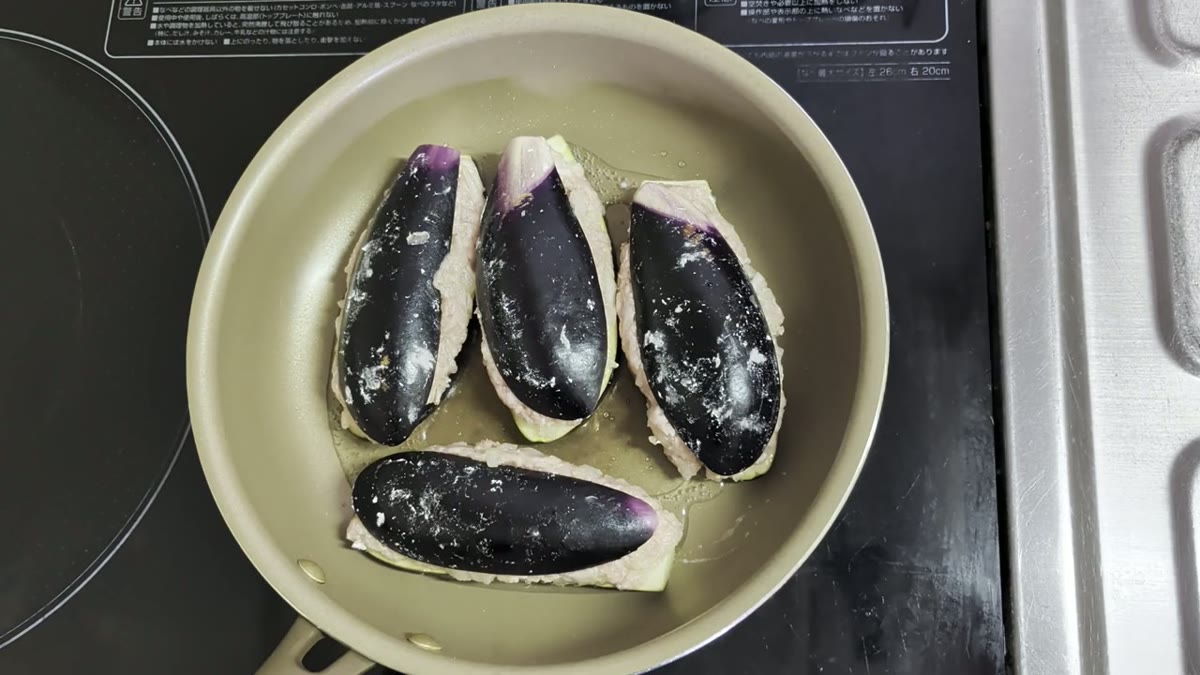 肉詰めなすをフライパンに並べ、焼き始める場面として適している。
